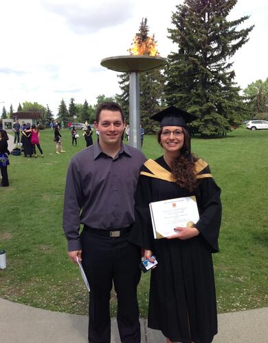 a young woman in a graduation cap and gown posing for a photo outdoors with a young man