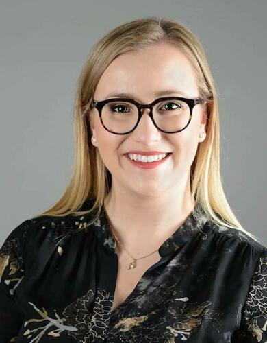 A woman with blonde hair and glasses smiles at the camera