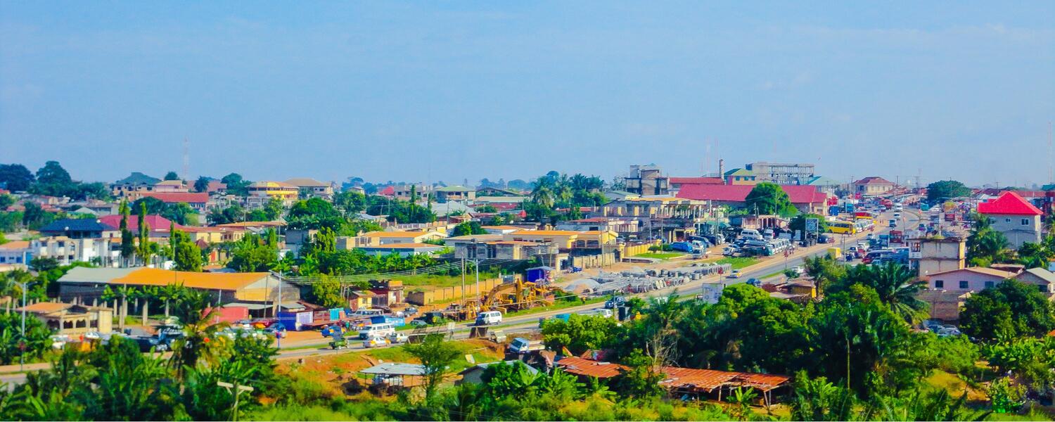 Skyline of Kumasi, Ghana; clusters of colourful buildings, lush green trees, and a clear blue sky