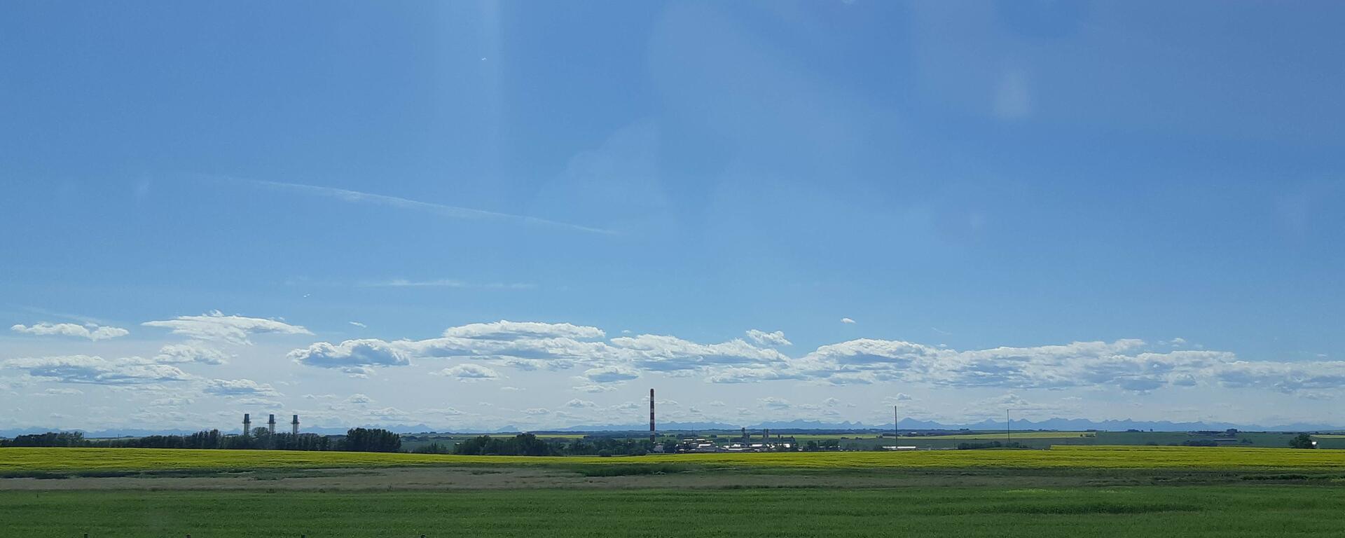 Sour gas plant in canola field with mountains in the background