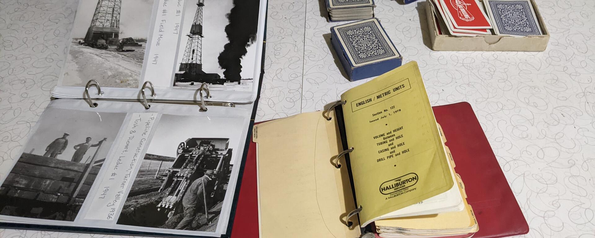 Photo album with Leduc oil find photos and other artefacts, including playing cards, notebook, on a table