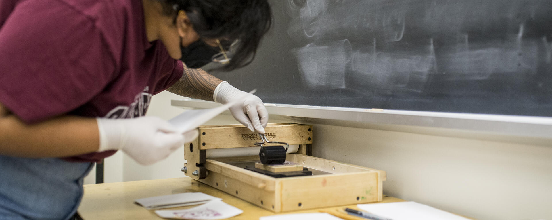 A young woman prints paper on a hand press with natural ink.