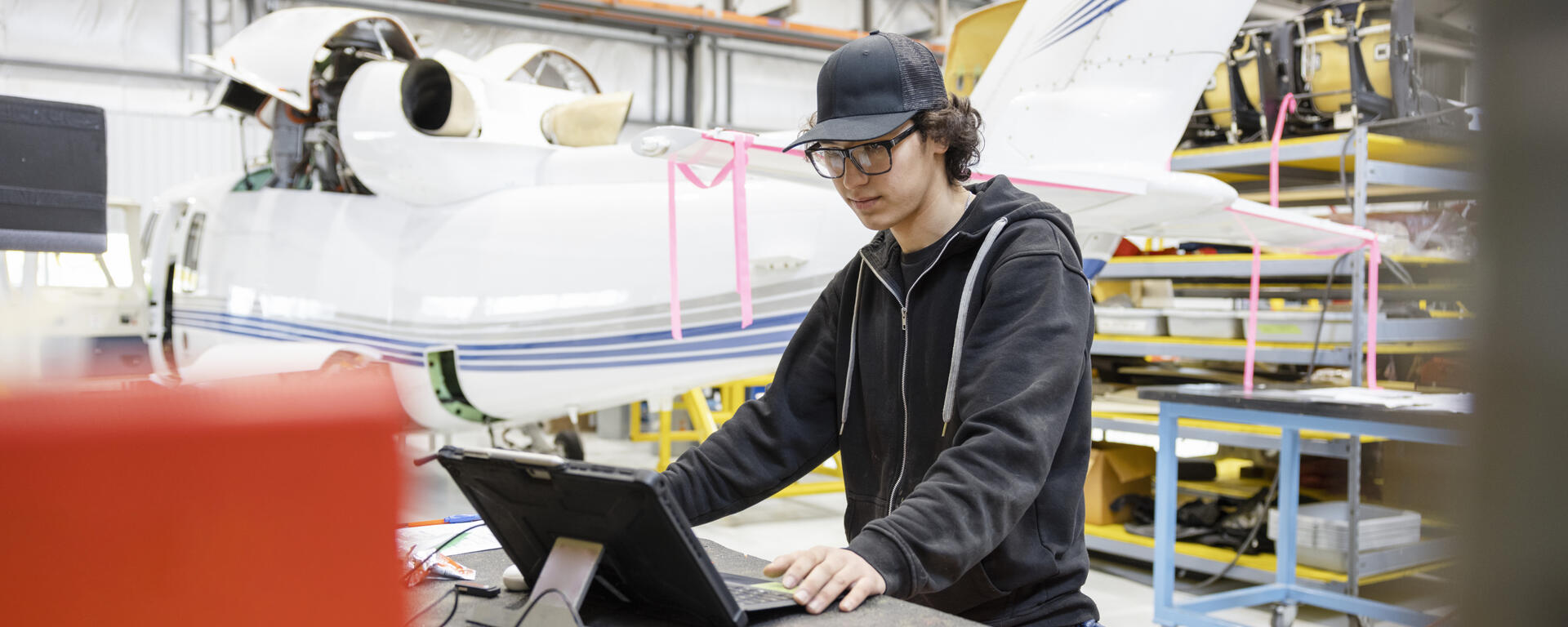 A student in an engineering workshop with a small plane behind them.