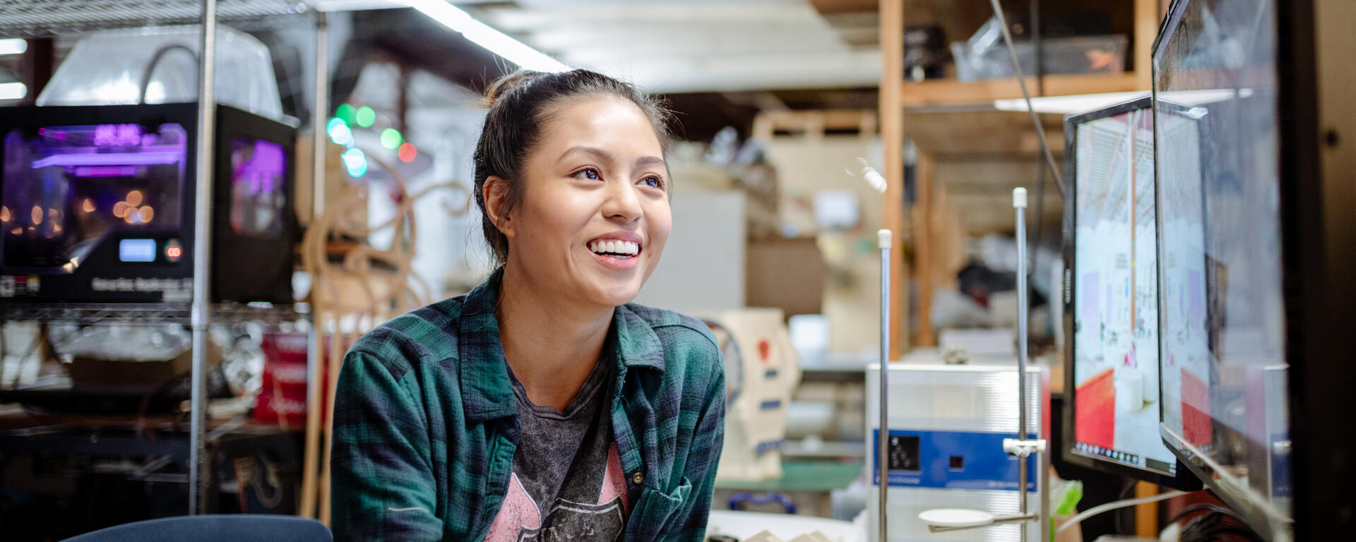 A student sitting in a computer lab leaning over a desk and smiling.
