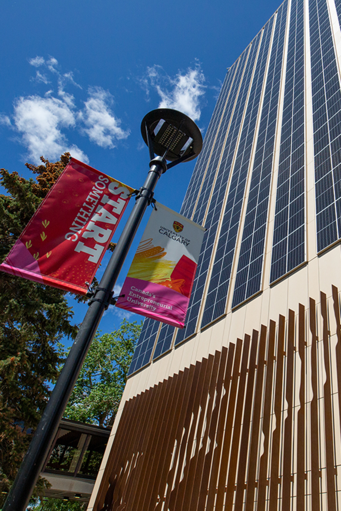 A view looking up at the social sciences building and a blue sky with whispy clouds. In the foreground are UCalgary "Start Something" and "Canada's Entrepreneurial University"