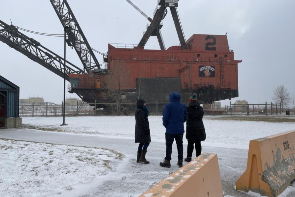 three people standing outside in front of an excavator in winter