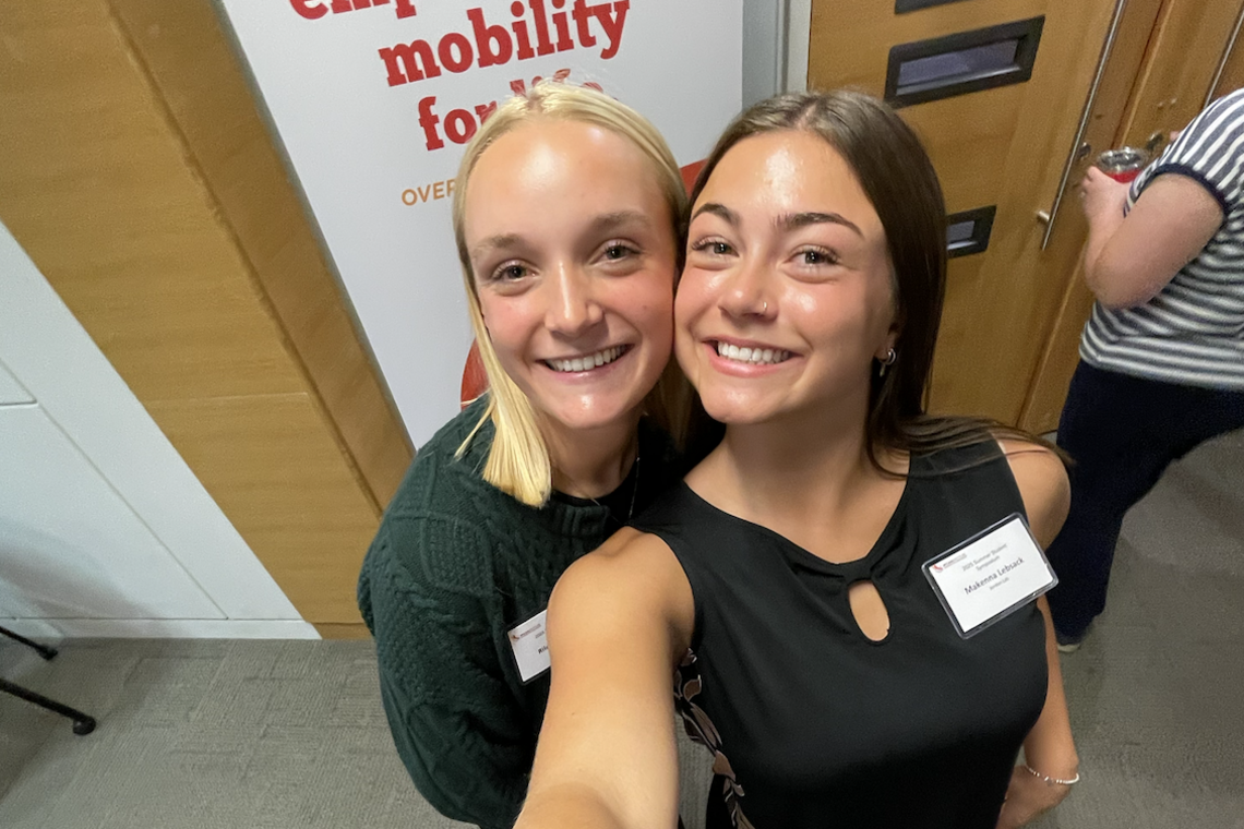 Makenna Lebsack taking a selfie with someone else in front of a research banner.