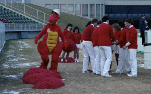 Dexter the dinosaur, 1985 Dexter, the University of Calgary Dinosaurs mascot with the university cheerleading team during a football game.