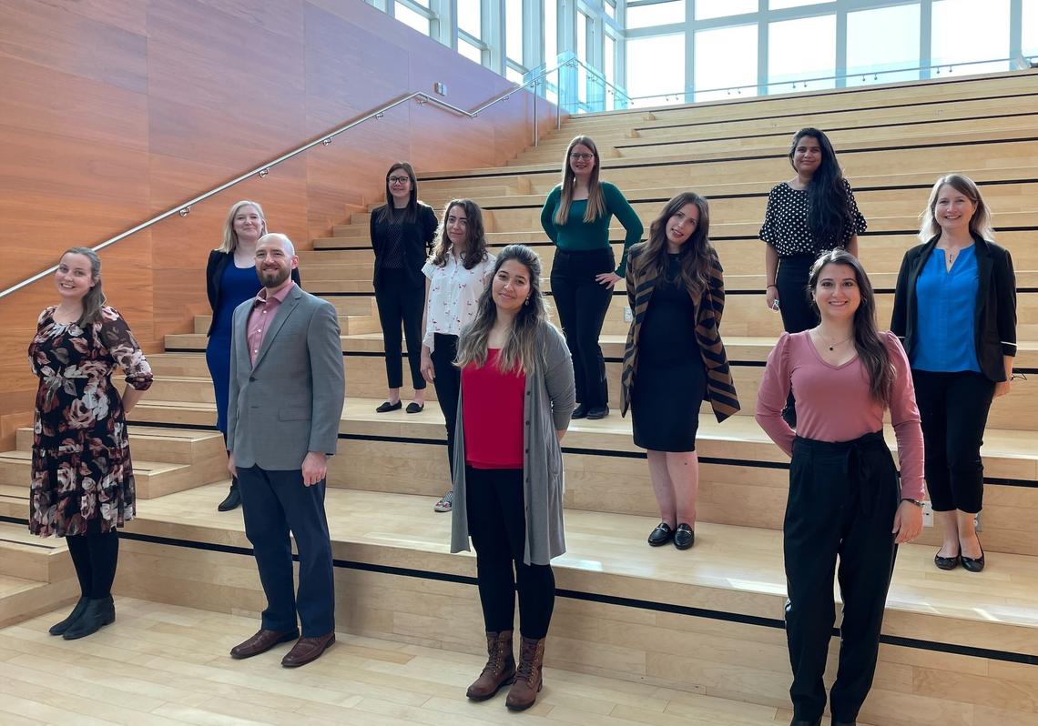 A group photo of 11 adults standing in a staggered line across several wooden steps
