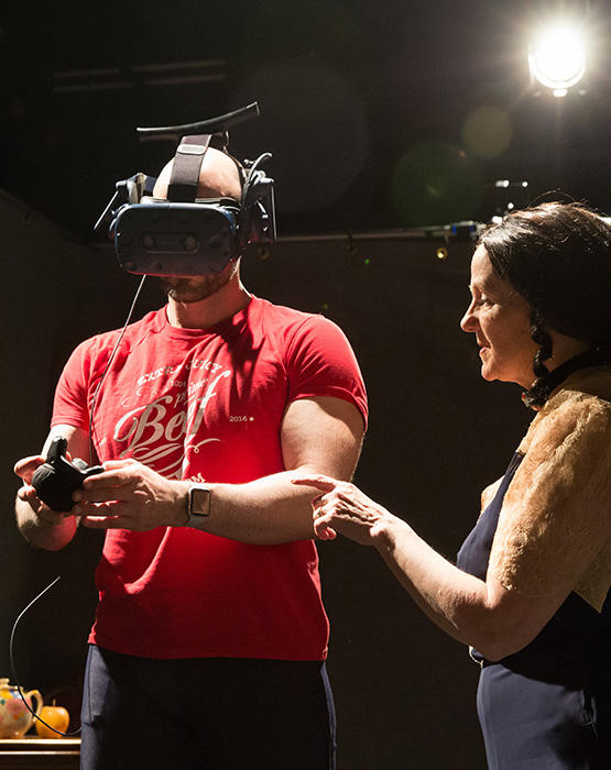 A woman directing a man using a VR headset.