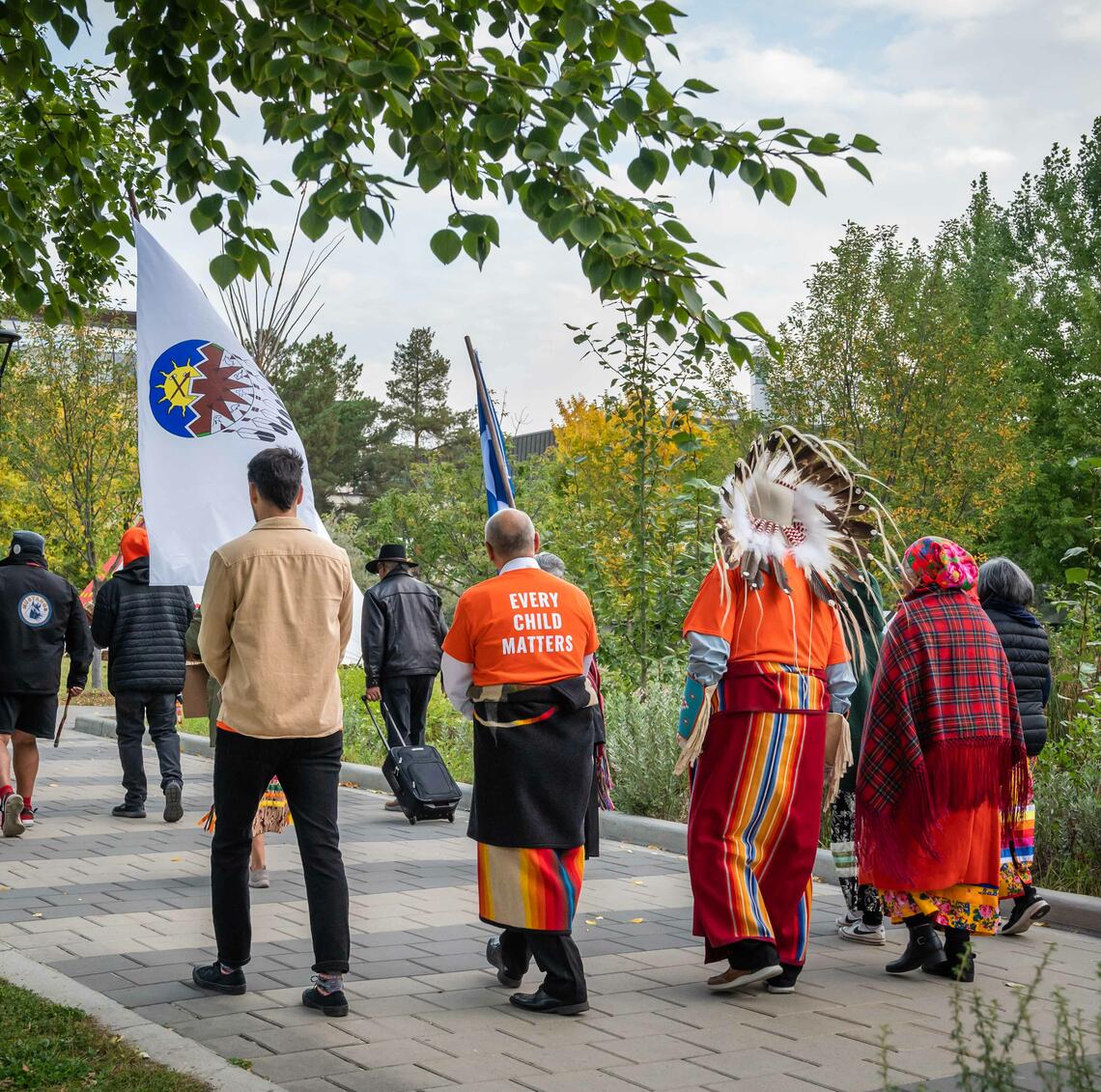 People walking along a path on campus with Elders Reg and Rose Crowshoe, and Dr. Michael Hart.