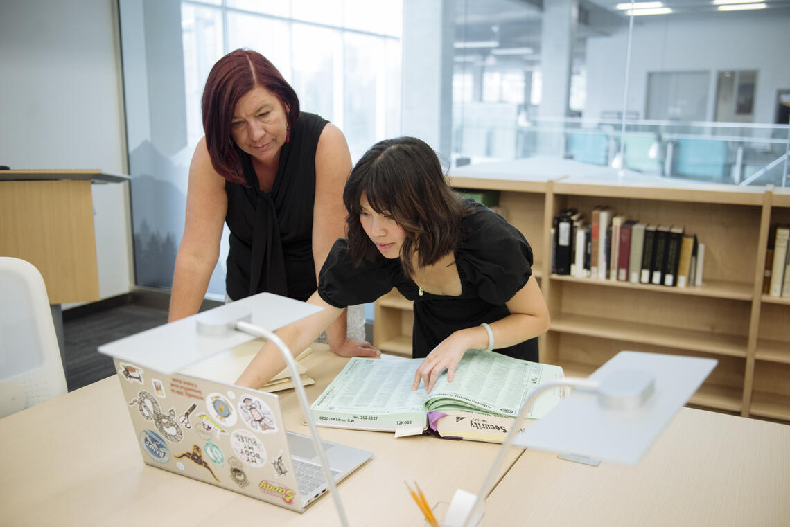 A supervisor and a student look over documents in the library.