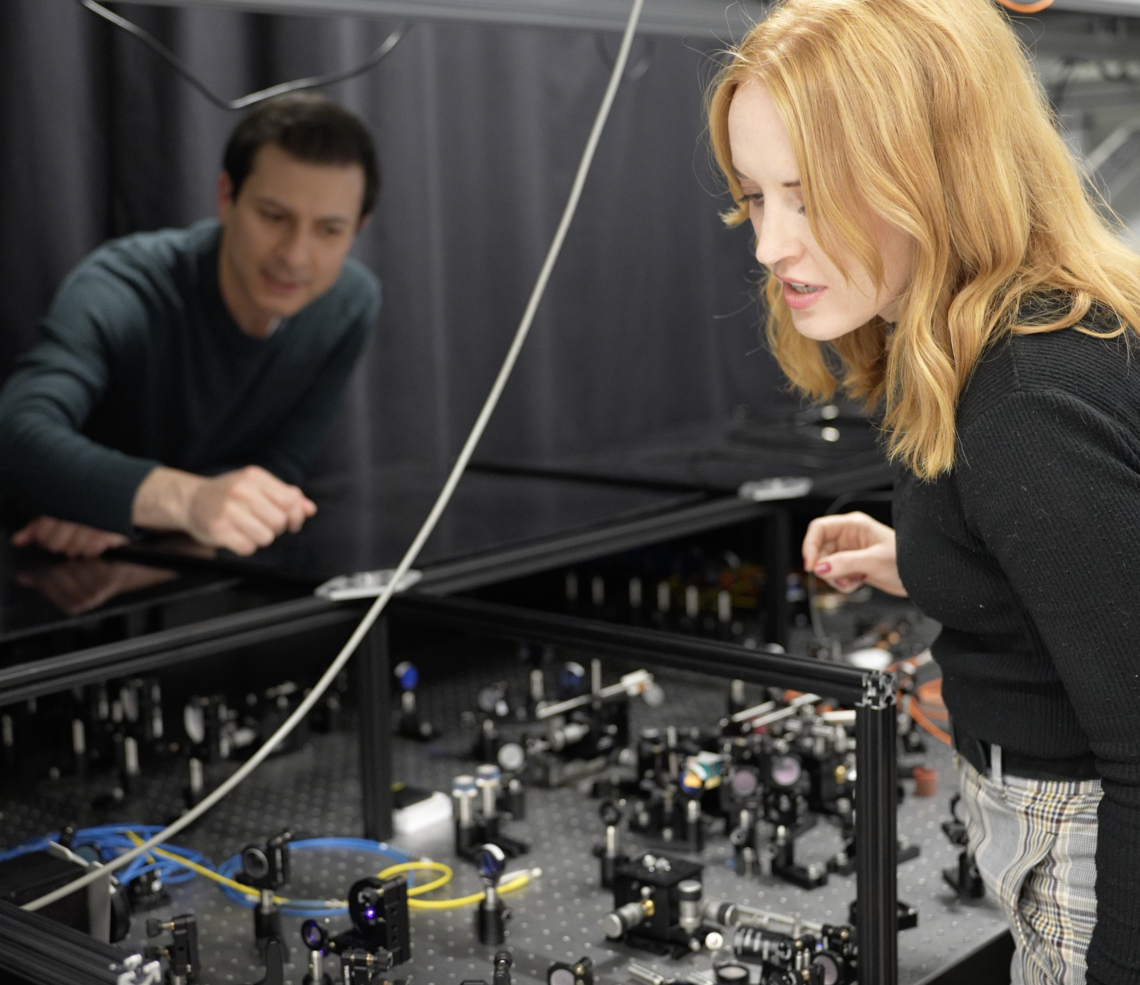 Two UCalgary researchers stand in a quantum lab interacting with equipment.