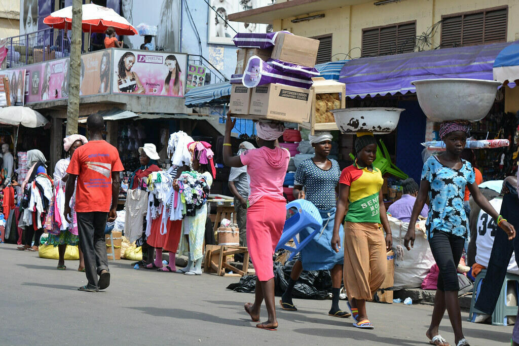 Women in colourful dresses carrying large bundles on their heads, walking through a busy street market