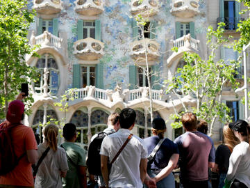 A view of the back of a group of people admire Casa Batllo(also in view), a beautiful building in Barcelona. 