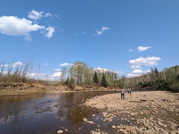 wide rocky beach along dark brown river with blue skies