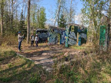 3 people standing in front of ruins, which include 4 walls now full of graffiti