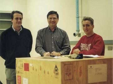 Three men standing around a large wooden box.