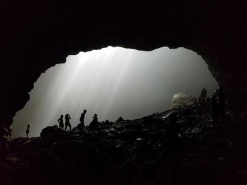 A dark photo, with far-off silhouettes of people walking through a cave in a spotlight