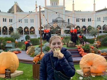Student eating a hotdog in a park decorated with pumpkins for the fall season