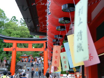 Beside a temple wall, with coloured flags hanging and a red arch ahead