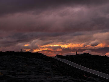 A row of students standing on the edge of volcanic rock with purple clouds in the background