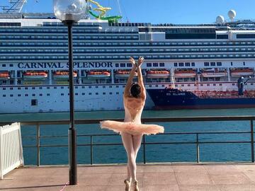 A ballerina in pink tutu twirls on a harbour in front of a cruise ship
