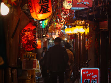 A dark narrow market street, with red lanterns overhead