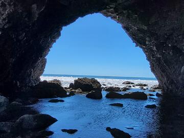 Standing inside a cave, looking out through a round opening towards blue water horizon