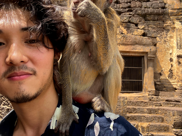 Person with short dark hair, looking at the camera with a small smile as a brown monkey perches on their shoulder