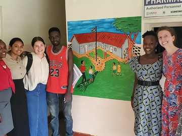 UCalgary and MUST students pose beside a wall painting at the clinic