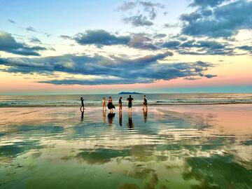 Pastel coloured clouds reflecting on students dancing on a shallow-water beach  