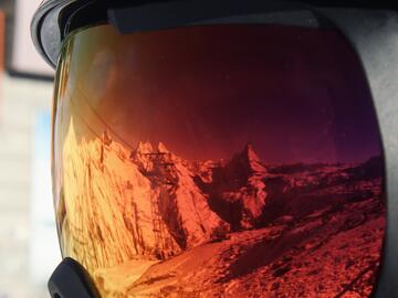 Reflection of mountains on a red pair of ski goggles