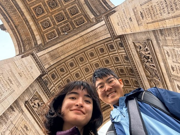 Two students looking down at the camera, smiling, with the Arc de Triomphe behind them