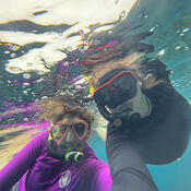 Two individuals posing just under the water in snorkel masks