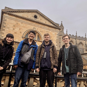 Four students standing in front of historical sandstone buildings