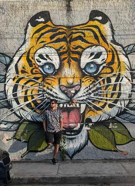 Student posing against a mural of a painted tiger