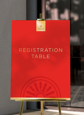 Red sign with gold details on an easel directing to a registration table