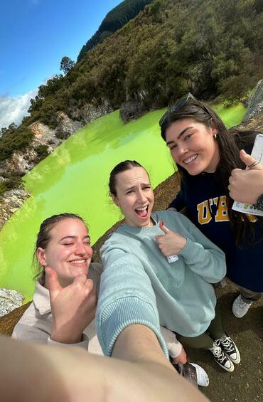 Selfie of three students in front of a volcano crater filled with lime green liquid