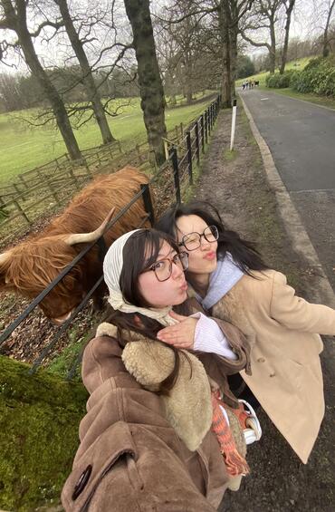 Selfie of two students with a hairy highland cow behind them