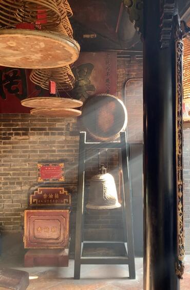 Standing in a dusty, sunlit room, with large bells hanging and smoke misting through the air