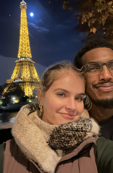 Two individuals posing at night in front of the glowing Eiffel Tower