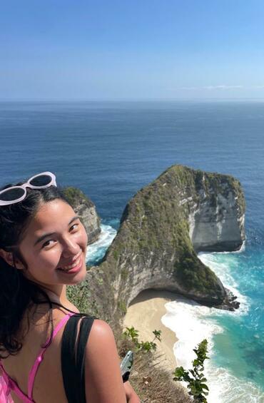 Student looking back at the camera with a grand view of rock and ocean behind them