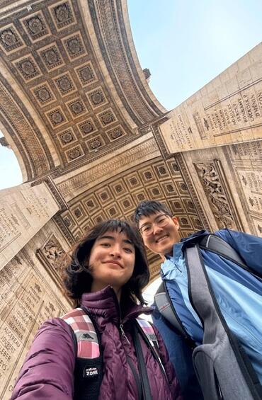 Students looking down at the camera with the arch of the Arc de Triomphe in the background