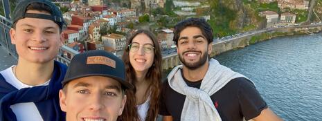 Four students posing on a bridge overlooking the river and city