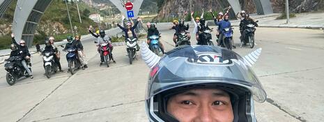 Selfie of a student in a helmet, with motorbike riders lined up in the background