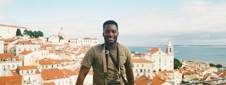 Student posing in front of view point of white buildings with orange roofs and ocean
