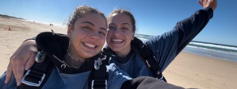 Two students posing with skydiving gear on the beach