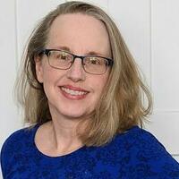 Astrid Eckstein, a fair skinned person with shoulder-length blonde hair and glasses, is smiling.