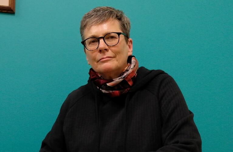 woman with grey short hair seated in front of turquoise wall